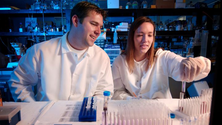 A student smiling holding a beaker and a classmate smiling on her right